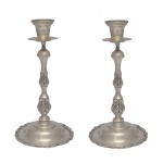 Par de castiçais de saia em prata mexicana, repuxada e cinzelada, ornados por folhagens gravadas. Hastes construídas em segmentos de balaústre, encimadas por bobeches cônicas. Bases circulares, levemente abauladas, bordadas por frisos com volutas florais. Contrastes mexicanos da prata 925 Sterling e marcas do prateiro JR. 26 x 13 cm (base). Peso 1k179  gramas.