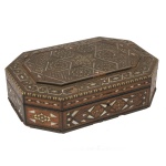 Caixa em madeira, de formato retangular chanfrada. Apresenta profusa decoração incrustada com frisos, medalhões e rosáceas em madrepérola e outros materiais. Tampa centralizando estrela de 6 pontas à frente, e verso seguindo o estilo. Marrocos ou Oriente Médio. (mínimas perdas nos embutidos).