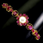 Majestosa pulseira em prata de lei espessurada a ouro amarelo, design moderno exclusivo de excepcional ourivesaria com preciosa cravação de Rubis de 6.0 x 4.0 mm, clássica lapidação oval brilhante, adornados por rico trabalho com linda Pérola de 8.0 mm e belíssima coroa de rubis de lapidações gota e diamante. Perfeito estado de conservação, sem uso. mede 19,5 cm de comprimento x 0,8 cm de comprimento. Origem África e Tailândia.