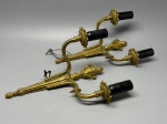 LUSTRE - Par de apliques duplos com decoração mitológica - Par de elegantes apliques de parede com dois braços cada, confeccionados em metal dourado, ricamente ornamentados com elementos clássicos e figuras mitológicas em relevo. Design de inspiração neoclássica, com hastes curvas, bobeches florais e terminais com pináculos e tochas estilizadas. Necessitam reparos elétricos. Med. 15x10 cm.