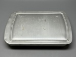 UTILITÁRIO VINTAGE  Travessa para sobremesas "DESSERTS" - Travessa antiga em alumínio com tampa original, modelo norte-americano utilizado em buffets e refeitórios, com a palavra DESSERTS em relevo na parte frontal. Design funcional com cantos arredondados e tampa plana ajustável. Peça de apelo colecionável, especialmente para composições retrô ou decoração temática.  Sinais naturais de uso e tempo. Med. 4x29x19 cm. Leve amassados.