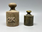 DIVERSOS - BALANÇA  Par de pesos antigos de ferro e latão - Conjunto composto por dois pesos antigos de balança:  Peso em ferro fundido marcado "2K" (2 kg), com pátina original do tempo. - Peso em bronze (provavelmente 1 kg), sem marca visível, com belo botão de pega e desgaste coerente com a idade. Peças utilitárias históricas com forte apelo decorativo e colecionável. Alt.12 cm (ferro) e 8 cm (bronze).