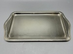 METAL - Bandeja retangular niquelada com bordas em relevo e delicado trabalho decorativo ao centro. Apresenta mancha no fundo. Med. 36x20 cm.