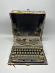 REMINGTON  Antiga máquina de escrever portátil com estojo original.Modelo portátil da consagrada marca americana Remington, com estrutura metálica e teclas redondas com anéis metálicos. Acompanha estojo rígido original com alça, bastante desgastado. A máquina está em estado de conservação regular, com partes faltantes, oxidação e desgastes, ideal para decoração vintage, cenografia ou restauro especializado. Med. 11x30x30 cm. Caixa com vestigios de ataque por cupim.