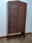 MOBILIÁRIO - ARMÁRIO ANTIGO DE DUAS PORTAS EM ESTILO COLONIAL/RÚSTICO - Robusto armário de época, confeccionado em madeira maciça com a autêntica pátina do tempo, que revela a beleza e a funcionalidade do mobiliário colonial brasileiro ou de fazenda. A peça possui duas portas de painéis planos, adornadas por dobradiças externas em metal escuro e um trinco simples, que complementam seu design rústico e tradicional. O topo em formato levemente inclinado ou de "chapéu de bruxa" confere uma característica particular ao móvel. Sustentado por pés integrados à própria estrutura, este armário é ideal para compor ambientes que buscam um toque de história e simplicidade elegante, como cozinhas, despensas ou salas com decoração campestre. Em ótimo estado geral de conservação, com sinais de uso que valorizam sua autenticidade.Med. 192x94x40 cm.