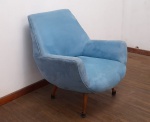 MOBILIÁRIO - POLTRONA ESTOFADA EM TECIDO AZUL COM DESIGN VINTAGE - Encantadora poltrona estofada, que se destaca pelo seu design elegante e convidativo, evocando a estética do mobiliário Mid-Century Modern ou dos anos 50/60. Revestida em um agradável tecido liso de tom azul (azul celeste ou similar), a peça oferece um visual vibrante e contemporâneo. Sua forma orgânica, com encosto e braços integrados, proporciona um conforto envolvente, enquanto os pés em madeira, discretamente inclinados, conferem leveza e o charme característico de sua época. Ideal para adicionar um ponto de cor e aconchego a salas de estar, escritórios ou quartos, integrando-se perfeitamente em ambientes modernos, retrô ou ecléticos. Em bom estado de conservação. Med. 82x70x57 cm. Marcas de uso.