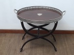 DIVERSOS - OBJETOS DE ARTE E DECORAÇÃO - BANDEJA OVAL EM METAL PRATEADO COM FUNDO EM MADEIRA E SUPORTE DOBRÁVEL - Elegante conjunto composto por uma bandeja oval em metal prateado e um suporte dobrável em madeira nobre. A bandeja, de design clássico, apresenta borda finamente trabalhada e alças laterais para manuseio, com um distinto fundo em madeira que confere um contraste sofisticado. O suporte, confeccionado em madeira de tonalidade escura, possui um engenhoso formato em "X" (cavalete), que não só garante estabilidade como também permite que a peça seja facilmente dobrada e guardada. Com dimensões totais de 58 cm de altura, 68 cm de largura (da bandeja) e 50 cm de profundidade (da bandeja), este conjunto é perfeito para servir com requinte em ocasiões especiais ou para atuar como uma charmosa mesa de apoio em ambientes clássicos e sofisticados. Em excelente estado de conservação, com a pátina natural do tempo que realça sua beleza.