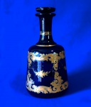 ANTIGUIDADE -  Magnífico decanter veneziano em cristal azul cobalto, com pintura decorativa em esmalte ocre e cobertura a ouro. Mede: altura 19,5 e 9,7 cm de diâmetro maior. Mínimas marcas do tempo, a tampa esta presa ao gargalo.