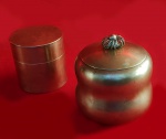 ANTIGUIDADE - Par de potiches com tampa em liga metálica dourada.  Um decorativo e outro tipo industrial, peça numerada. Medem respectivamente: 10 x 10 cm e 8 x 8 cm. No estado.