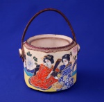 JAPÃO - Importante peça em porcelana decorada com pinturas típicas, gueixas e florais com relevo. Vaso com alça em trança de bambu. Assinado ao fundo com marca de reconhecido fabricante. Mede 14 cm de altura e 16 cm de diâmetro. Bem conservado. Antiguidade.