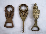 Três (03) abridores de garrafa em bronze dourado de diferentes formatos e tamanhos, dois com figuras de alce, um com armadura e um com escudo da cidade de Budapeste.