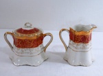 ROYAL BONE FINE CHINA  22kt gold- Açucareiro e cremeira em porcelana na cor branca, decorado ao centro com cena galante, borda recortada com faixa bordô com farta douração a ouro em guirlandas. Marcado na base. Med. cremeira 11 cm alt. Apresenta alguns desgastes na douração.