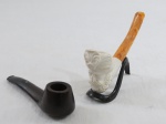 Dois (2) cachimbos sendo: um em madeira da Marca Berman Séc XX ( 13,5 cm comprimento), um em espuma do  esculpido com figura masculina, acompanha suporte ( 14 cm comprimento). Ambos sem Uso.