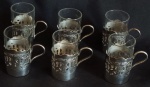 Lote contendo seis copinhos em vidro translucido, com suporte confeccionado em metal prateado, com rico detalhes de arabescos e pega lateral. Medida: 7x4cm.