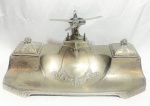 W.M.F - Espetacular, imponente e raro tinteiro alemão, Art Deco, circa 1930, em metal espessurado a prata W.M.F, magnificamente cinzelado, encimado por Cena de Avião, articulável. Contrastado. Med 16x35x22 cm. Obs: Falta recipientes em cristal, apresenta discretas marcas do tempo.