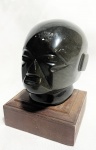 ARTE MEXICANA - "Divindade" Antiga e rara escultura regional mexicana, anos 50, em pedra possivelmente Hematita polida esculpido a mão, apoiada sobre base em madeira nobre, representando Cabeça de Divindade. Med 12x8x8 cm.