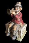 Linda escultura Musical confeccionada em biscuit representando palhaço tocando corneta sentado sobre caixote, Peça musical. Medidas: 18x17,5x27cm. Obs:.  não testada.