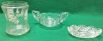 Lote com três peças de vidro sendo, da  esquerda para a direita: Um pote de vidro transparente, com formato cilindrico e delicados desenhos florais brancos gravados; Uma molheira de vidro com duas alças e borda ondulada e  uma petisqueira em vidro, decorado  com padrões geométricos intrincados e também com borda ondulada. Usados. Sem trincas, lascados ou quebras.