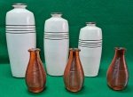 lote com 2 conjuntos de vasos decorativos, totalizando 6 peças. . Na fileira de trás,  três vasos brancos de cerâmica com superfície lisa e listras pretas horizontais próximas ao topo. Na frente, aparecem três vasos menores, de vidro, com textura canelada em um tom marrom-avermelhado. Usados. Sem trincas, quebras ou lascados.