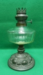 Luminária de mesa à querosene. Base em metal e reservatório em vidro, sem o queimador original. Aparentemente adaptado para eletricidade. Sem cúpula e sem a manga. Medidas: 25cmA x 14cmD.