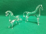 Par de esculturas em cristal, representando cavalos. a maior mede 10 A x 11,5 C x 3 L e apresenta dois pequenos lascados, um na ponta da orelha e outro na ponta do focinho, a menor mede 8 A x 9,5 C x 2,5 L.