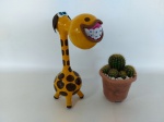 ESCULTURA - GIRAFA: Escultura de mesa representando girafa com aparelho nos dentes, feitos de cabeça. Medida: altura: 32 cm.