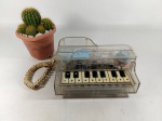 TELEFONE - ANTIGO: Antigo e diferente telefone de mesa representando piano, executado em acrílico transparente, não testado. Medidas: altura: 9 cm, largura: 17 cm e comprimento: 21 cm.