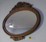 Antigo espelho no formato oval com moldura em madeira entalhada com frisos na borda e acabamentos com laçarotes e folhagens, medindo cm X cm.