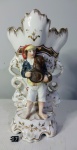 Vista Alegre, Portugal  Início século XX em belíssima floreira em formato de ânfora ovalada, decorada figura de homem com cesto, branco e dourado com alças em forma de seres mitológicos. Marca na base. Altura de 25 cm e medindo 14 x 10 cm. OBS: Apresenta pequena perda em um dos pés e marcas como fios de cabelo.