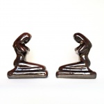Antigo par de esculturas de figuras femininas com pernas dobradas e braços cruzados em cerâmica vitrificada em tom de castanho escuro. Exemplar em excelente estado. Dimensões: 17 cm x 28 cm x 10 cm.