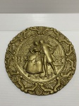 Medalhão de metal revestido de dourado decorado com cena galante. Dimensões: 28 cm / 1,5 kg.