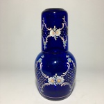 Antiga e delicada moringa em vidro azul, estilo veneziano, decorada com flores, volutas e estilizados pintados à mão. Realces em Ouro 24k. Exemplar em excelente estado. Dimensões: garrafa 19 cm / copo 9,5 cm.
