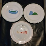 Treis pratos rasos em porcelana branca decorada em policromia com pontos turísticos do Rio de Janeiro, todos com suporte de arame para pendurar. Diam. 25cm.