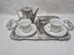 Lote de bandeja, bule, porta guardanapos e manteigueira em aço inox e 2 xícaras de chá em porcelana. Medindo a bandeja 40cm x 30cm x 52,5cm alça a alça.