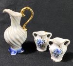 Mini jarra e dois vasinhos em porcelana. Medidas: jarra 14 cm de alt. e vasos 7 cm de altura. Possui pequena lasca no bocal do vasinho e jarra