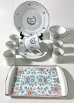 Lote diversos em porcelana contendo:  Duas xicaras de chá uma com pires e prato de sobremesa com friso prateado e dizeres Bodas de Prata, Cinco xícaras de cafezinho em porcelana branca com friso prateado sem suportes, pequena travessa com decoração floral. Medidas da travessa 12 x 21 cm