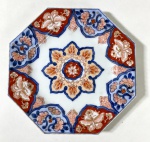 CIA DAS ÍNDIAS- IMARI-JAPÃO SÉCULO XIX - Prato de formato octogonal, em porcelana policromada no estilo Imari, decorado em vermelho-ferrugem, azul cobalto e dourado. No centro, composição floral em forma de roseta, cercada por reservas com motivos florais e estilizações orientais. A paleta e a simetria ornamental revelam a elegância típica da produção japonesa destinada à exportação no período Edo/Meiji. Medidas: