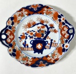CIA DAS ÍNDIAS- IMARI-JAPÃO SÉCULO XIX - Centro de mesa na forma redonda  em porcelana policromada Imari, com forma recortada de pegas laterais vazadas, decorado em azul cobalto, vermelho-ferrugem e dourado. A aba apresenta reservas florais estilizadas, enquanto o centro traz composição com elementos orientais e ramos floridos. Bordas recortadas com duas alças vazadas, de formato orgânico. Medidas: