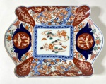 CIA DAS ÍNDIAS- IMARI-JAPÃO SÉCULO XIX - Travessa retangular de bordas recortadas, em porcelana decorada no tradicional estilo Imari, com paleta em azul cobalto, vermelho-ferrugem e dourado, apresentando reservas florais e composição central com flores e folhagens. Peça de grande presença decorativa, típica da produção oriental destinada à exportação. Medidas: