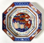 CIA DAS ÍNDIAS- IMARI-JAPÃO SÉCULO XIX - Centro de mesa octogonal de bordas recortadas, em porcelana decorada no tradicional estilo Imari, com paleta em azul cobalto, vermelho-ferrugem e dourado, apresentando reservas florais e composição central com flores e folhagens. Peça de grande presença decorativa, típica da produção oriental destinada à exportação. Medidas: