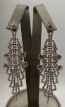 Par de brincos em metal prateado cravejado por strass. Comprimento: 9cm