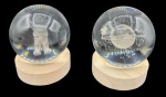 Dois pesos de papel em cristal com base em madeira com luz interna. Sendo um deles, com figura de astronauta e outro de Saturno com estrelas na parte interna. Altura (com base): 9cm