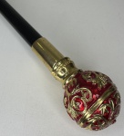 Bengala com castão no bola ricamente ornamentada com esmalte vermelho em metal dourado. Altura: 92,5cm. Possui lâmina interna, 29cm.