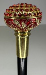 Bengala com castão no feitio de bola ricamente trabalhada em metal dourado incrustado por cristais e esmalte vermelhos. Altura: 90,5cm. Possui lâmina interna, 29cm.