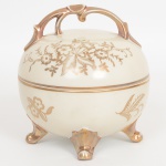 PORCELANA ALEMÃ, uma (1) bomboniere com tampa, modelagem esférica, ornamentação vegetalista a ouro sobre fundo na tonalidade creme, pega da tampa relevada na forma de galho, pés terminando em volutas, marcado MARCHANDISE ALLEMANDE  KRIS  MARK  MADE IN GERMANY (referencia a produtos fabricados na Alemanha), medindo 13,5 cm diâmetro e 15 cm altura, vide foto.