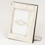 FOTOGRAFIA, um (1) porta-retratos confeccionado em metal prateado, relevado em orquídea no padrão Art Nouveau, envidraçado, marcado LE LIS BLANC CASA, medindo 11 x 8 cm, não aparenta ter sido usado, ainda com a etiqueta, vide foto.