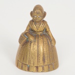 BRONZE, uma (1) pequena sineta de mão, representando figura feminina com trajes de Chapeuzinho Vermelho, medindo 7 cm altura, sinais de uso, vide foto.