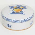 PORCELANA PORTUGUESA, uma (1) caixa com tampa, ornada com vaso de flores na tonalidade azul e amarela sobre fundo branco, manufatura VISTA ALEGRE (fundada em 1824, pelo negociante, lavrador, industrial e político, José Ferreira Pinto Basto, através de alvará concedido por D. João VI, tendo seu fundador associado a fábrica os seus 15 filhos, ficando a sociedade denominada Ferreira Pinto & Filhos; cinco anos mais tarde recebe o título real pelo reconhecimento de sua arte e sucesso, ficando conhecida como Real Fábrica da Vista Alegre, começou no fabrico de vidros enquanto se empenhava em esforços para a produção de porcelana, os primeiros ensaios conseguidos foram imperfeitos denominado loiça de pó de pedra, através de boas relações com a fábrica francesa de Sevres conseguiu as receitas para o fabrico de porcelana, somente em 1832, por sorte, é encontrado um jazigo de caulim situado em Aveiro, próximo a Ílhavo, a partir desta data o fabrico de porcelana foi se aperfeiçoando em Portugal, 1851 expôs com sucesso no Palácio de Cristal em Londres; 1852 D. Fernando II visita a fábrica e encomenda uma baixela completa; 1867 recebeu sua primeira premiação na Exposição Universal de Paris; 1880 interrompe a produção de vidros para se dedicar exclusivamente a porcelana; 1964 inauguração do Museu Histórico da Vista Alegre; ainda em funcionamento), medindo aproximadamente 6,5 cm diâmetro, vide foto.