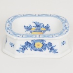 PORCELANA PORTUGUESA, um (1) saleiro, ornado com vaso de flores na tonalidade amarela e azul sobre fundo branco, manufatura VISTA ALEGRE (fundada em 1824, pelo negociante, lavrador, industrial e político, José Ferreira Pinto Basto, através de alvará concedido por D. João VI, tendo seu fundador associado a fábrica os seus 15 filhos, ficando a sociedade denominada Ferreira Pinto & Filhos; cinco anos mais tarde recebe o título real pelo reconhecimento de sua arte e sucesso, ficando conhecida como Real Fábrica da Vista Alegre, começou no fabrico de vidros enquanto se empenhava em esforços para a produção de porcelana, os primeiros ensaios conseguidos foram imperfeitos denominado loiça de pó de pedra, através de boas relações com a fábrica francesa de Sevres conseguiu as receitas para o fabrico de porcelana, somente em 1832, por sorte, é encontrado um jazigo de caulim situado em Aveiro, próximo a Ílhavo, a partir desta data o fabrico de porcelana foi se aperfeiçoando em Portugal, 1851 expôs com sucesso no Palácio de Cristal em Londres; 1852 D. Fernando II visita a fábrica e encomenda uma baixela completa; 1867 recebeu sua primeira premiação na Exposição Universal de Paris; 1880 interrompe a produção de vidros para se dedicar exclusivamente a porcelana; 1964 inauguração do Museu Histórico da Vista Alegre; ainda em funcionamento), medindo 10,5 x 8 x 3,5 cm, vide foto.