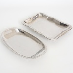 AÇO INOX, duas (2) travessas distintas: 1 oval, lisa, marca MERIDIONAL, medindo 29 x 16,5 cm; 1 retangular, borda relevada em volutas, marca WOLFF (tradição desde 1894), medindo 27,5 x 20 cm, sinais de uso, vide foto.